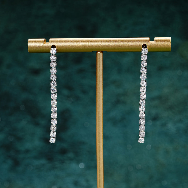  Infinity Line Ohrringe auf Schmuckhalter in 18K Gelbgold – lange, funkelnde Moissanite-Steine, elegantes Design von NOBEL Jewelry.